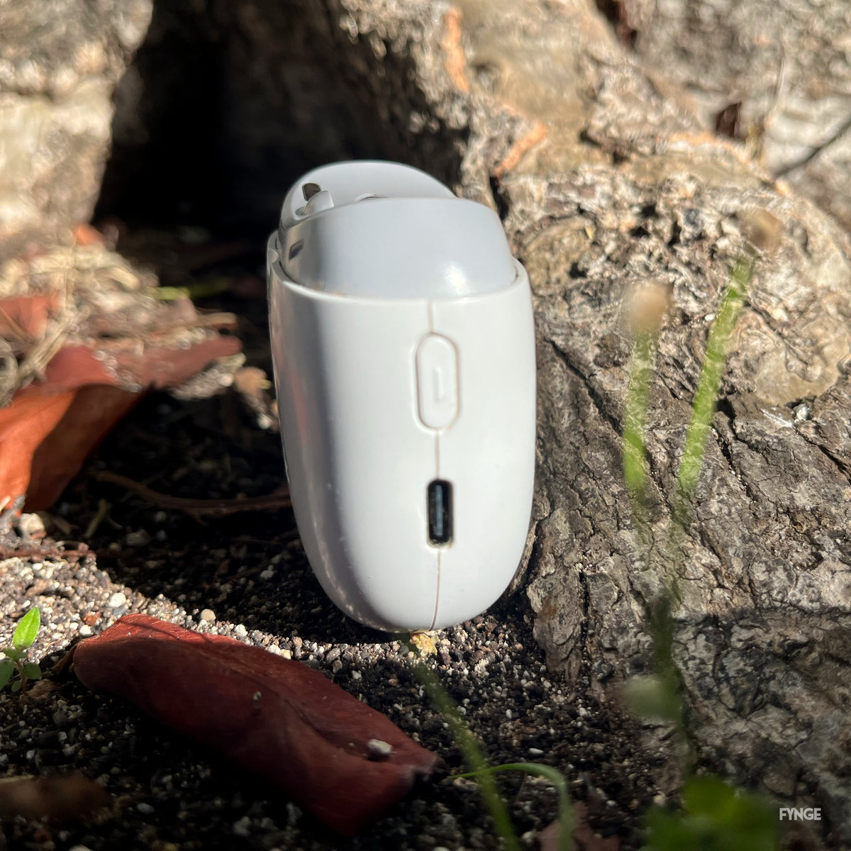 Side view of the FYNGE trimmer against a tree root, showing the charging port