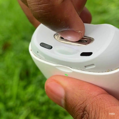 A fingertip resting in the opening on top of the white FYNGE trimmer, held outdoors over grass.