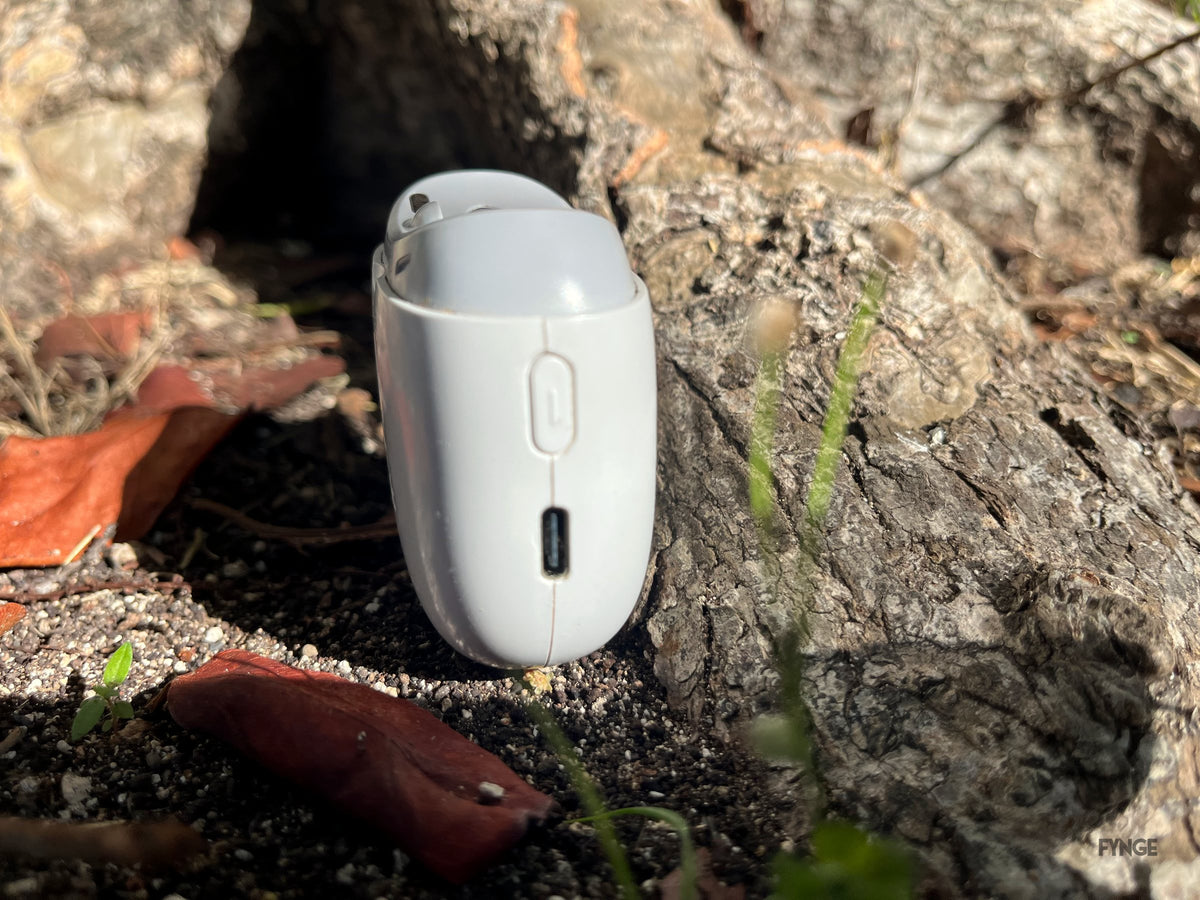 Side view of the FYNGE trimmer standing against a tree root, showing the power button and charging port